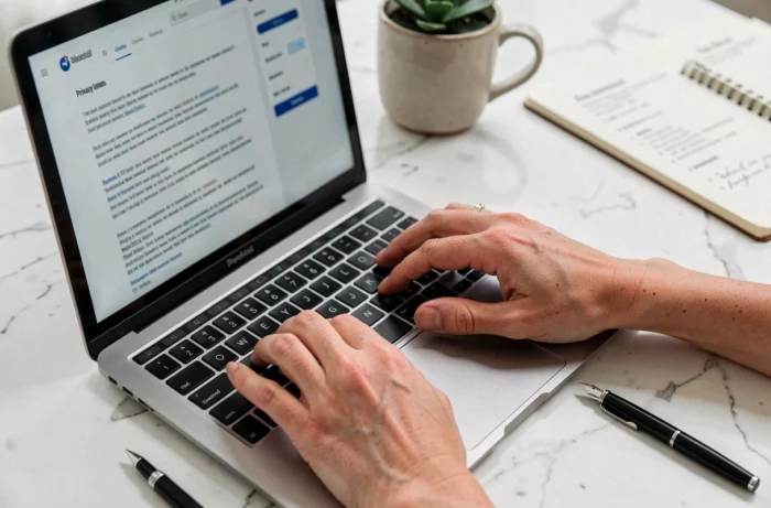 Mains d'une juriste saisissant une politique de confidentialité sur un ordinateur portable avec des documents légaux sur un bureau en marbre