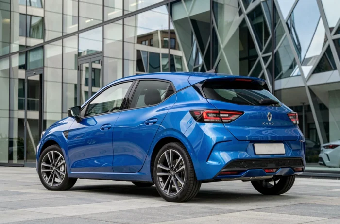 Nouvelle Renault 5 électrique bleu vif en milieu urbain moderne, vue trois quarts arrière soulignant le design rétro-futuriste et les lignes aérodynamiques contemporaines du véhicule